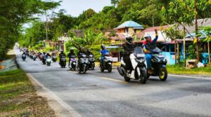 Ratusan riders Yamaha tampak konvoi santai melintasi jalan poros dengan latar perkampungan dan pepohonan hijau saat agenda SUNMORYGAB jelang Ramadan.