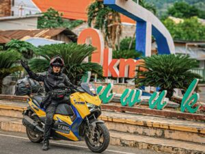 Om Daeng mengendarai Yamaha XMAX berwarna kuning-biru saat singgah di salah satu titik ikonik Luwuk dalam rangka touring Jelajah Sulawesi.