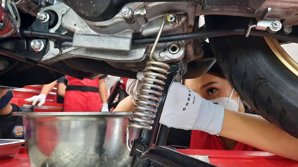 Mekanik melakukan pengecekan bagian bawah motor saat servis, memastikan komponen motor tetap dalam kondisi prima setelah perjalanan jauh.
